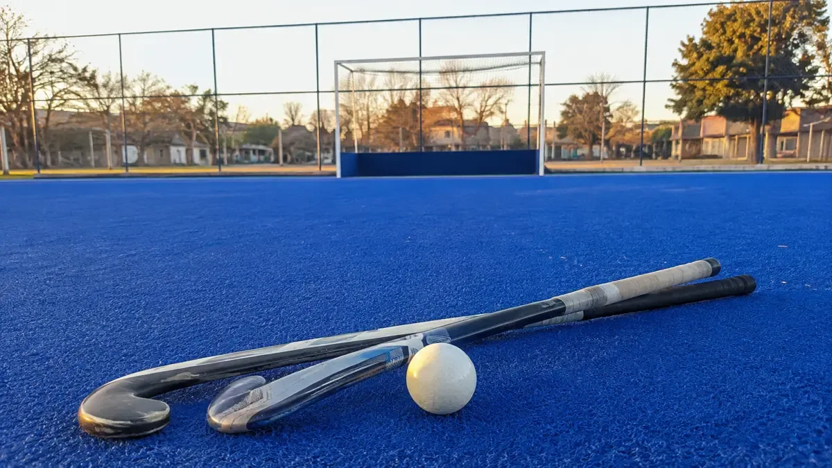 Cancha sintética de hockey con palos y pelota, sin jugadores a la vista.